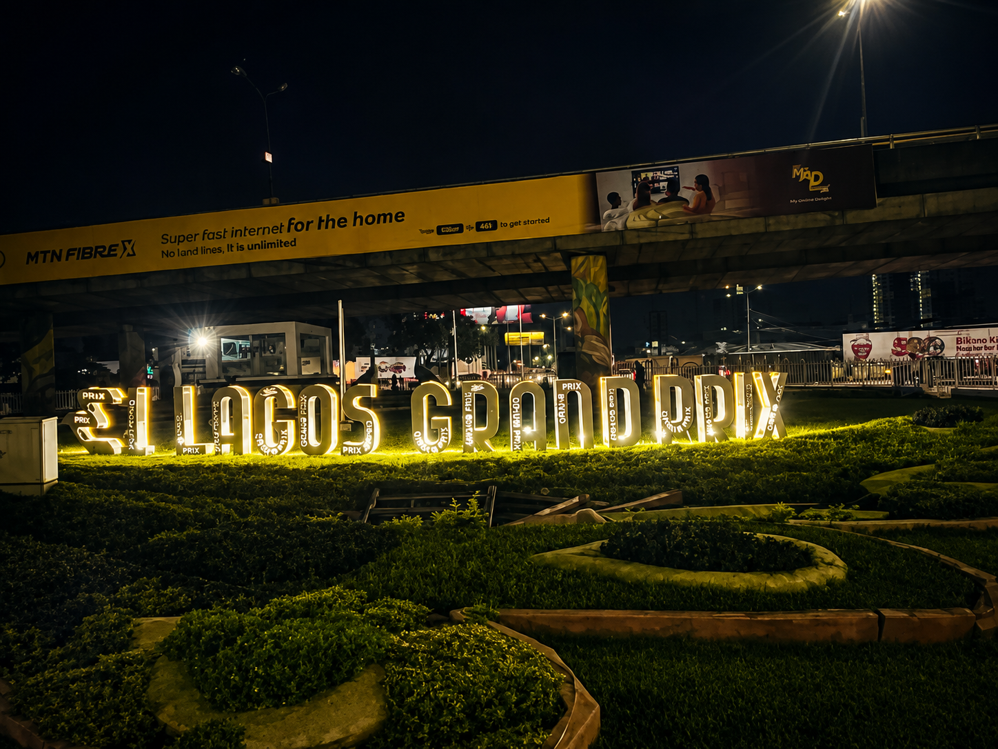 Illuminated Lagos Grand Prix lettering in an outdoor landscaped setting at night